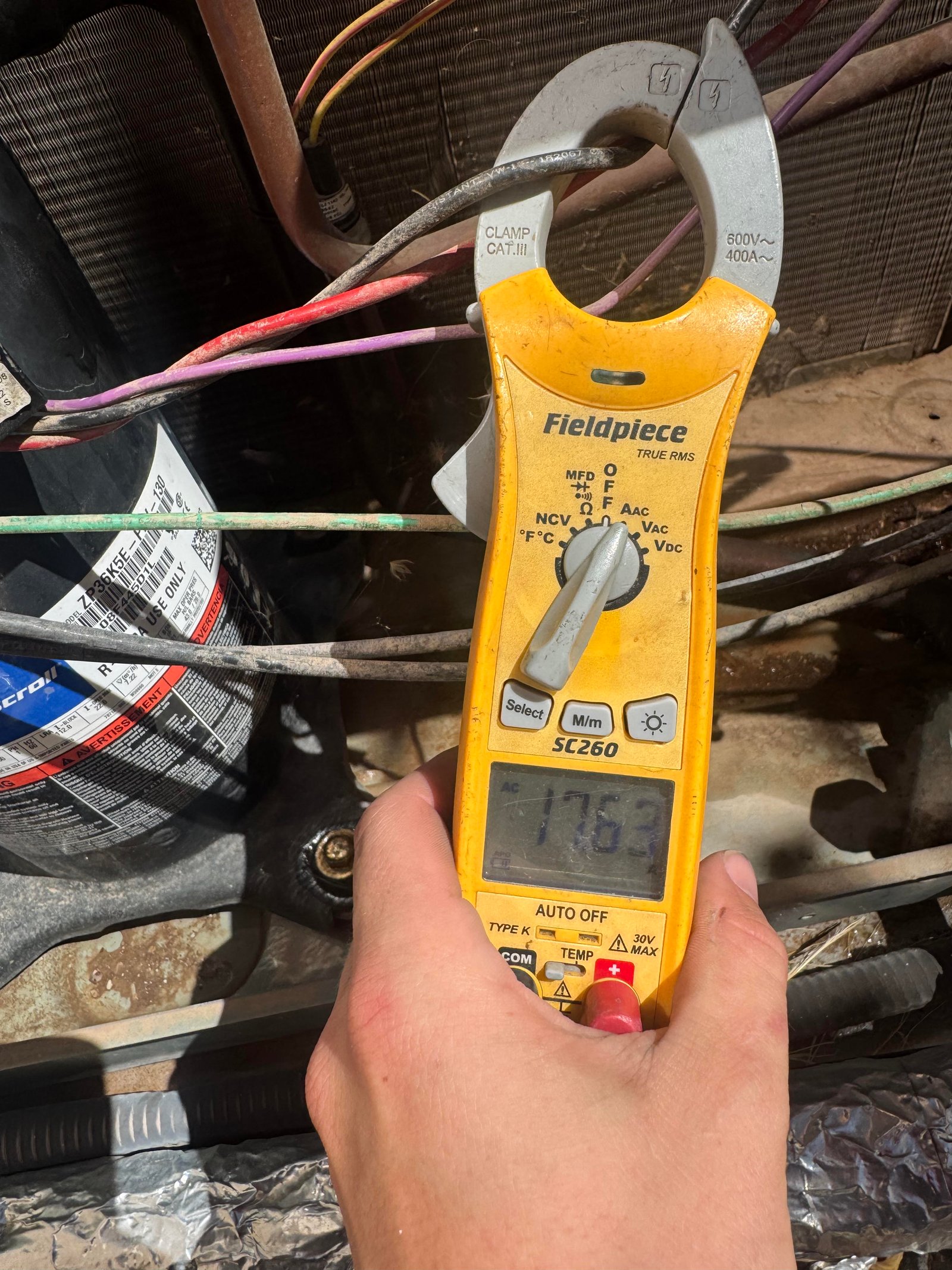 Technician measuring compressor amp draw on voltmeter during HVAC service in Tucson, AZ